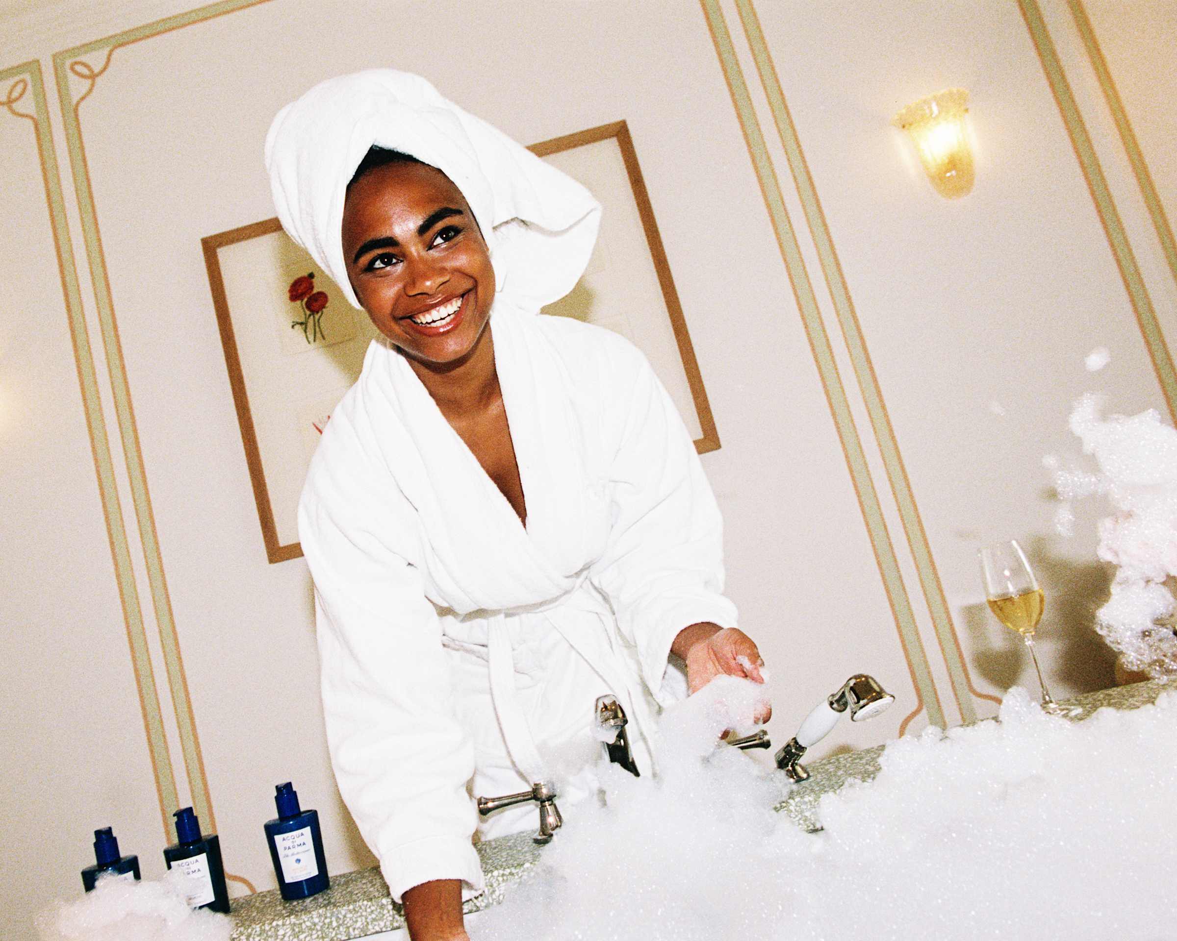 Guest in a bathrobe beside a bubble-filled bath in a Splendido junior suite bathroom