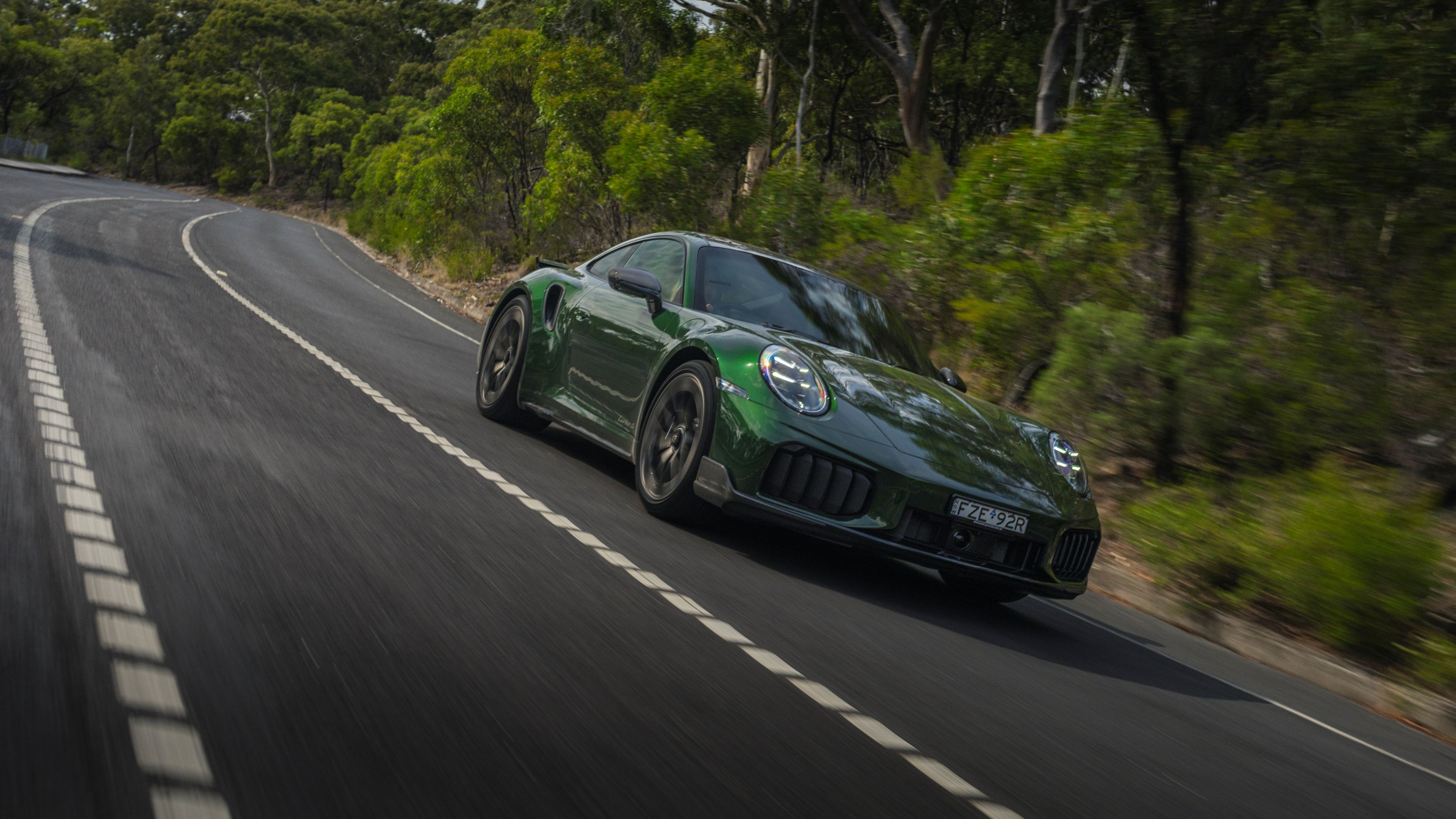 Current 911 Turbo S family in the official green front three-quarter driving view