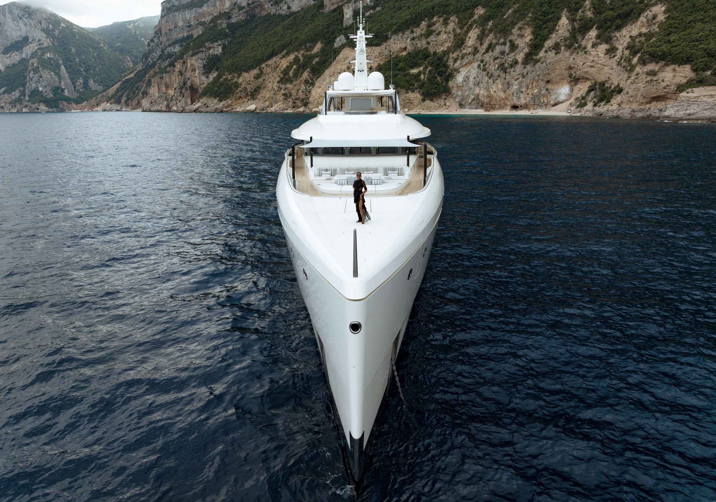 Yacht photographed near a rocky coastline in Burgess’s official charter-management imagery; not an availability statement.