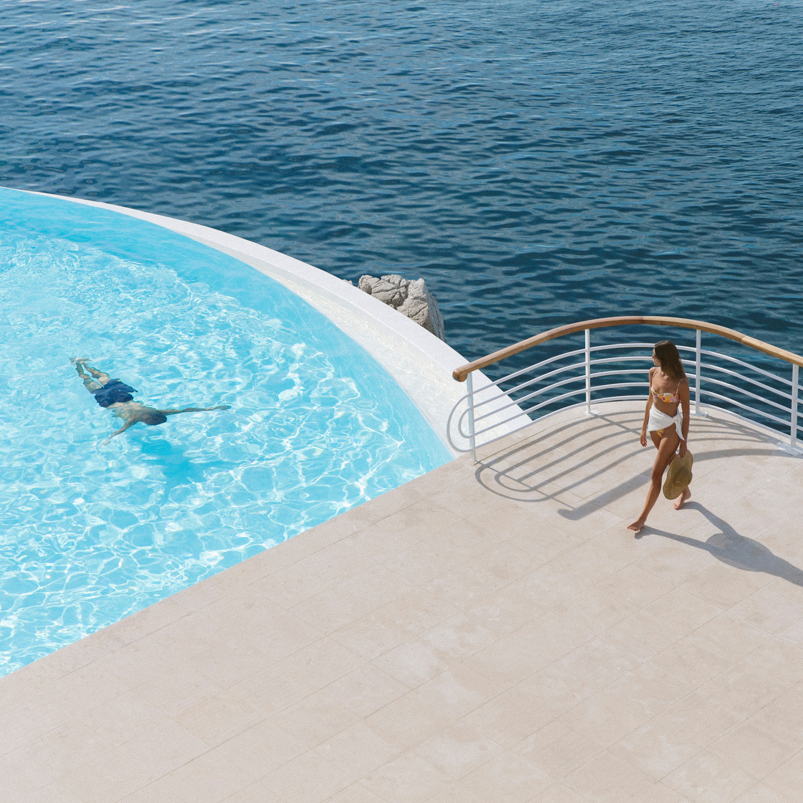 Official lifestyle photograph at the saltwater pool, with the sea immediately beyond.